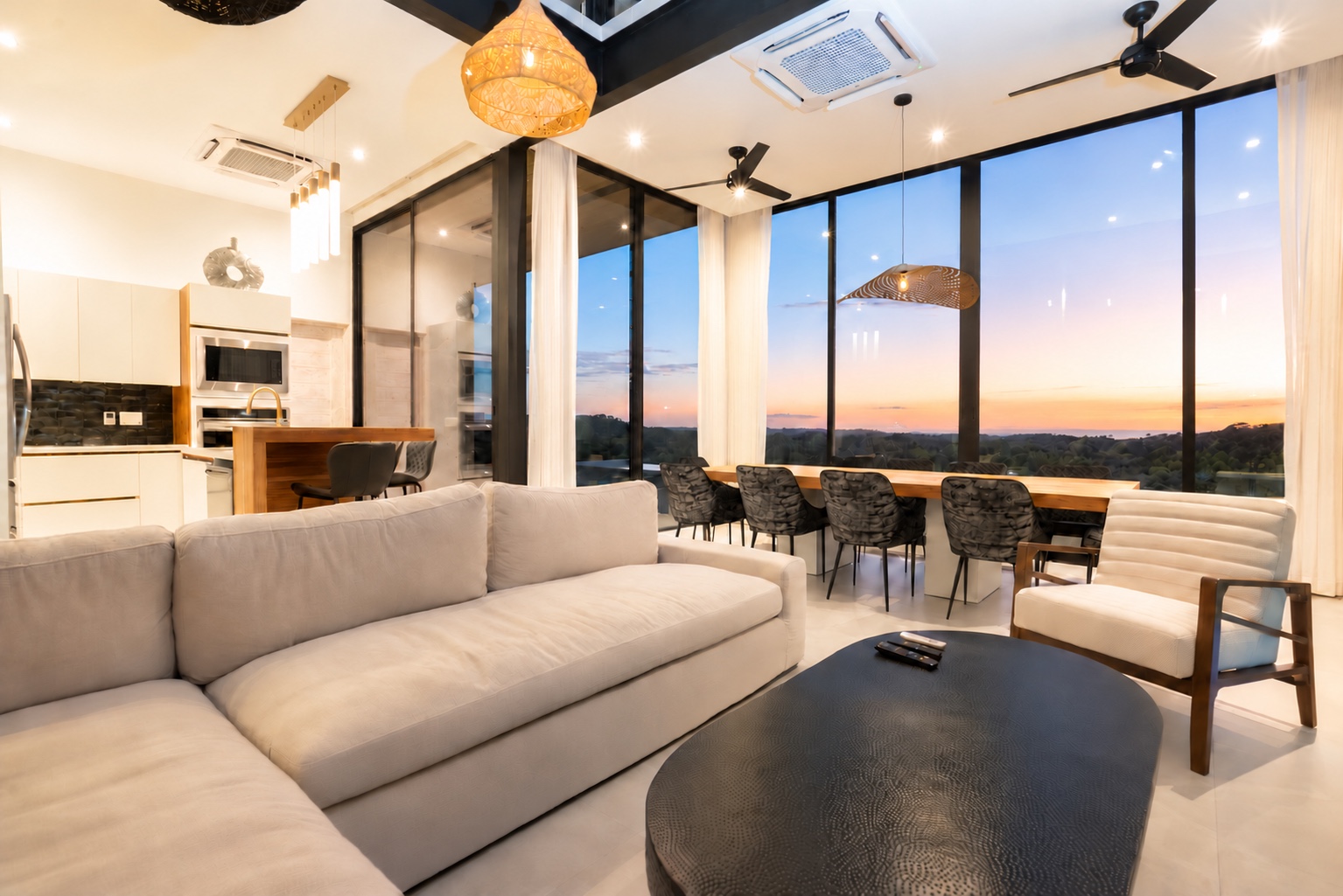 Open-plan living room and kitchen with floor-to-ceiling windows overlooking the Pacific at sunset